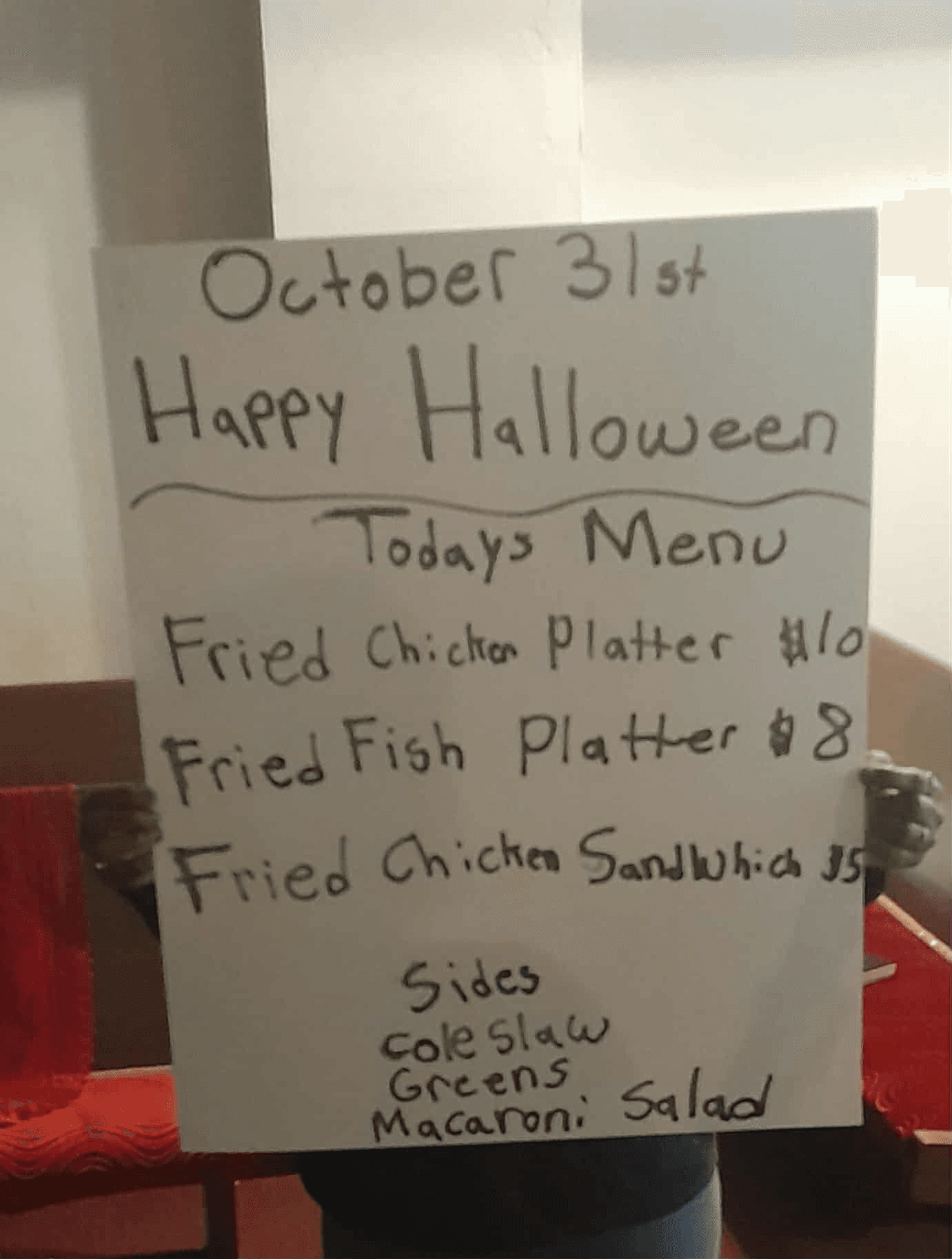 Handwritten Halloween menu sign showing meal options and prices for October 31st including fried chicken platter, fried fish platter, and chicken sandwich with sides